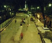 119757 Afbeelding van een bevroren Oudegracht te Utrecht, bij avond, met schaatsende mensen, vanaf de Jansbrug, uit het ...